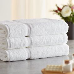 three white towels stacked on top of each other in front of a vase with flowers