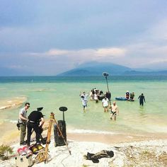 a group of people standing on top of a sandy beach next to the ocean with instruments