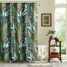 a bathroom with a shower curtain that has green and blue leaves on it, along with a rug