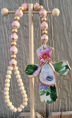 a cross made out of shells and flowers on a stand with beaded necklaces