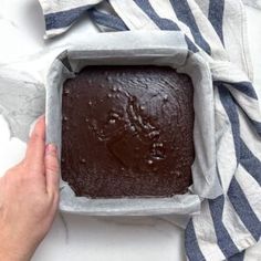 a person holding a pan filled with brownies on top of a table next to a striped towel