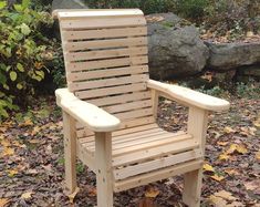 a wooden chair sitting on top of leaves in front of a rock wall and trees