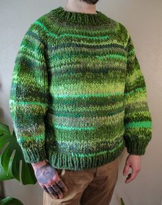 a man wearing a green and black sweater standing in front of a potted plant