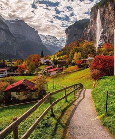 a scenic view of a mountain village with a path leading up to the mountains and houses