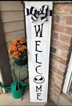 a wooden welcome sign sitting on the side of a building with flowers in front of it