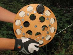 a person holding a wooden object with holes in it's center and two gloves on the other hand