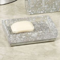 a square soap dish sitting on top of a marble counter next to a silver container