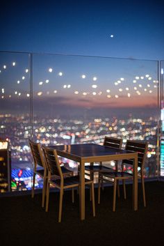 a table and chairs on top of a balcony overlooking a city at night with lights in the distance