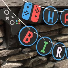 a birthday banner with video game controllers hanging from it's side next to a stone wall