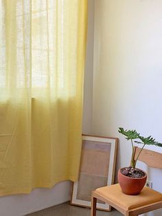 a potted plant sitting on top of a wooden table next to a yellow curtain