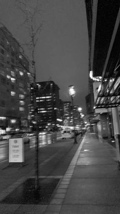 black and white photo of city street at night with buildings in the backround