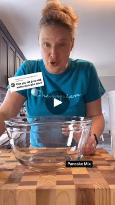 a woman in a blue shirt standing at a wooden table with a glass bowl on it