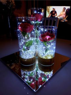 three glasses filled with water and roses on top of a table in front of a tv