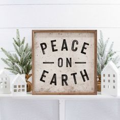 a wooden sign that says peace on earth with small white houses and evergreens in the background