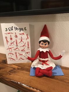 an elf doll sitting on top of a wooden table next to a sign that says elf yoga