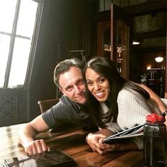 a man and woman sitting at a wooden table with an open book in front of them