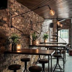 the interior of a restaurant with brick walls and wooden tables, stools and plants