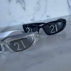 two pairs of sunglasses with diamond embellishments on them, one is black and the other is white