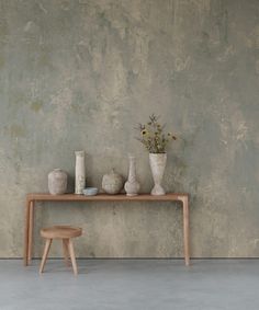 a table with vases and flowers on it in front of a concrete wall background