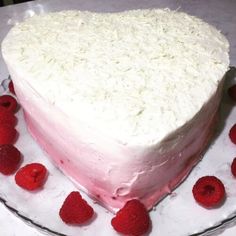 a heart - shaped cake with white frosting and raspberries on a plate