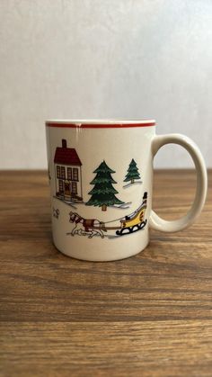 a coffee cup with a christmas scene on it sitting on top of a wooden table