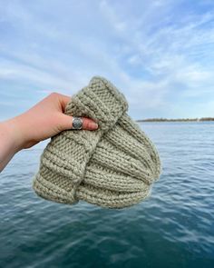 someone is holding up a knitted object in their hand over the edge of a body of water