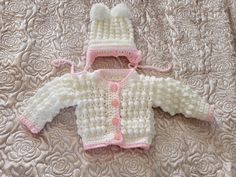 a crocheted baby sweater and hat laying on a bed