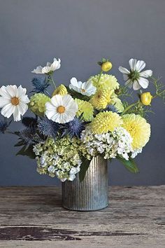 a vase filled with lots of white and yellow flowers on top of a wooden table