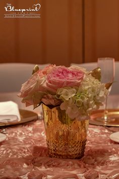 a vase filled with pink and white flowers sitting on top of a table next to plates