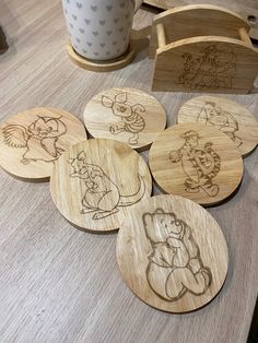 wooden coasters with cartoon drawings on them sitting on a table next to a cup