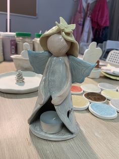 a ceramic angel figurine sitting on top of a table next to paint bowls