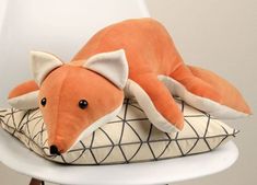 an orange stuffed animal laying on top of a white chair with a black and white pillow