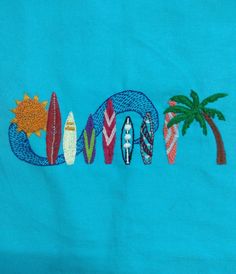 a blue shirt with surfboards and palm trees embroidered on the front, along with words that spell out love