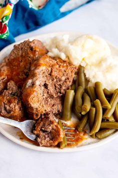 a white plate topped with meat, green beans and mashed potatoes