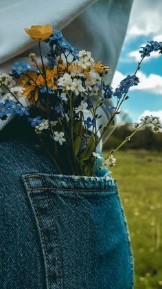 a person with their back to the camera holding flowers in his jeans pocket while standing in a field