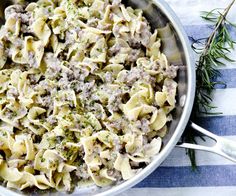 a pan filled with pasta and meat on top of a striped table cloth next to a spoon