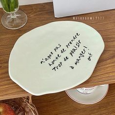 a white plate with writing on it sitting on a wooden table next to a vase