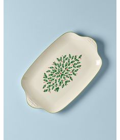 a green and white platter with holly designs on the side, against a blue background