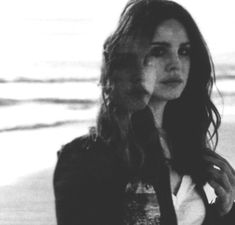 a black and white photo of a woman standing on the beach with her hair blowing in the wind