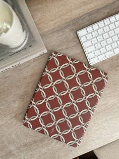 a red and white notebook sitting on top of a wooden desk next to a keyboard