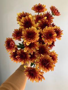 a hand holding a bouquet of flowers in front of a white wall with red and yellow petals