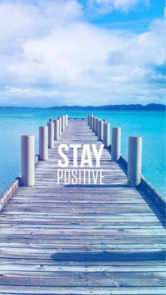 a wooden dock with the words stay positive on it in front of blue sky and water