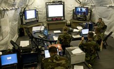 soldiers sitting at desks with laptops and monitors