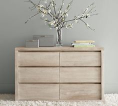 a wooden dresser sitting on top of a white rug next to a vase filled with flowers