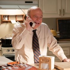 an older man talking on a cell phone while holding a wooden block in his hand