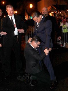 two men in suits and ties are being assisted by another man who is kneeling down