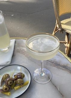 a table topped with a plate of food next to a glass filled with liquid and olives