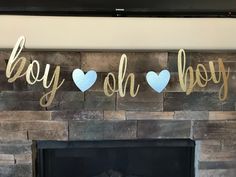 a fireplace with some paper hearts hanging from it's mantle and the words boy on baby spelled in gold foil