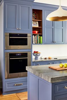 a kitchen with blue cabinets and marble counter tops, an island in the middle has fruit on it