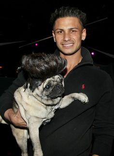 a man holding a small pug in his arms